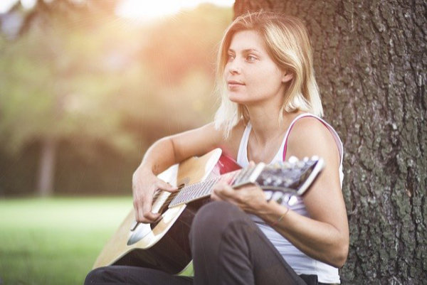 Frau beim Gesangstraining online mit Gitarre in einem Park